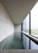 A modern and minimalist interior space featuring a long rectangular pool of water alongside a large window. The design is characterized by clean lines, polished concrete surfaces, and an overall sense of tranquility. Natural light softly illuminates the room through the window, creating reflections on the water.