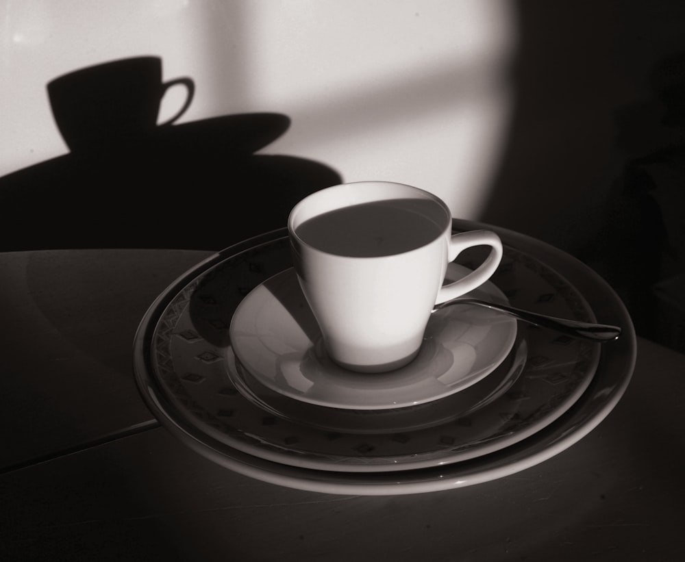 grayscale photography of mug with spoon on top of saucer and plate