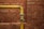 A yellow metal pipe runs horizontally along a red brick wall with a 90-degree elbow joint, showing signs of age and wear.