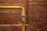 A yellow metal pipe runs horizontally along a red brick wall with a 90-degree elbow joint, showing signs of age and wear.