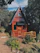 Cozy wooden A-frame cabin nestled among lush green trees with a sunset sky in the background.