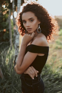 woman wearing black off-shoulder top with left hand under chin during daytime