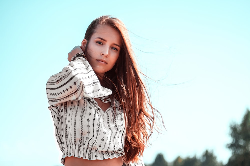 woman wearing white and black long-sleeved crop top with right hand on neck