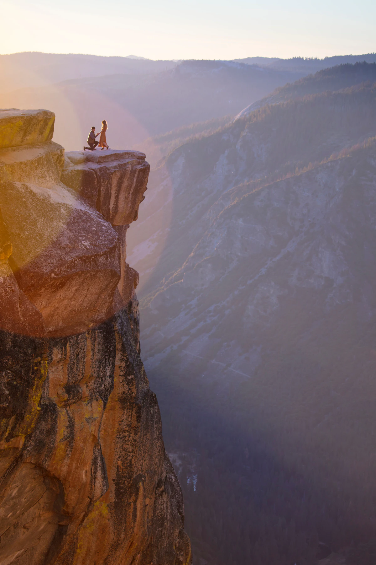 A man proposing to a woman on a rocky ledge at sunset