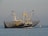 A trawler with a large blue hull and the identification number WR22 sails on calm waters. The fishing vessel is equipped with extended nets on both sides, suggesting that it is in the process of fishing. In the background, a few seagulls are flying, and a yellow buoy is visible near the ship.