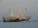 A trawler with a large blue hull and the identification number WR22 sails on calm waters. The fishing vessel is equipped with extended nets on both sides, suggesting that it is in the process of fishing. In the background, a few seagulls are flying, and a yellow buoy is visible near the ship.