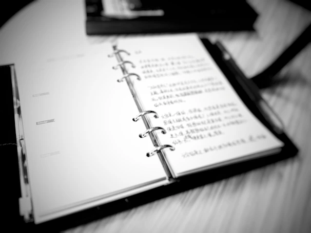 High contrast photo of a hand gripping a worn notebook, pages filled with blunt, handwritten notes.