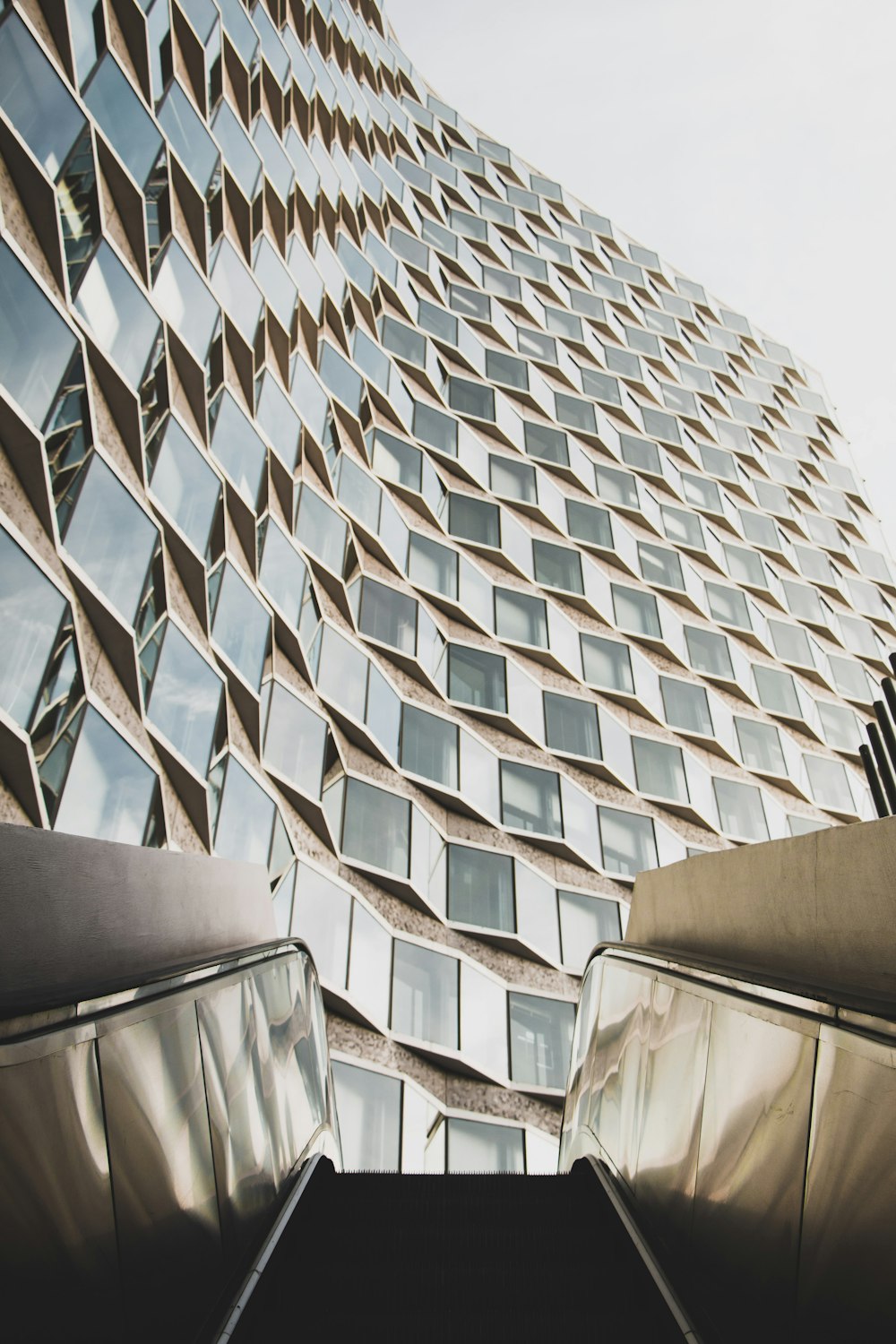 Photographie en contre-plongée d’un immeuble de grande hauteur en verre depuis un escalator
