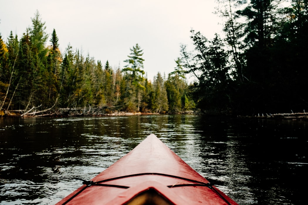 Red canoe floating down a river from the perspective of the rower seat