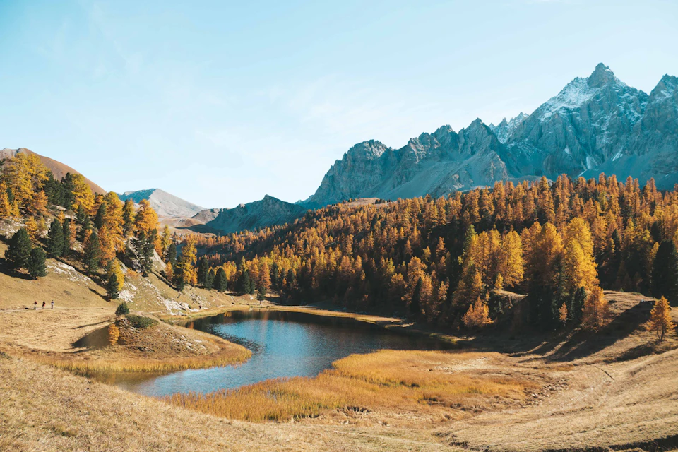 Serene mountain landscape with calm lake surrounded by trees and shrubs in autumn/winter