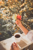 Close-up of a hand holding a warm cup of spiced cider with falling leaves in the background