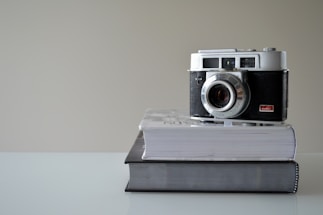 A minimalist black-and-white photo of a vintage camera resting on a clean white table.