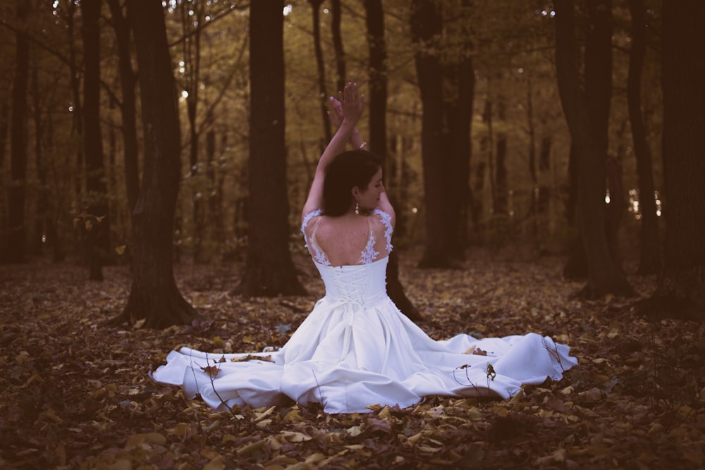 나뭇잎 더미에 앉아있는 흰색 민소매 드레스를 입은 여자