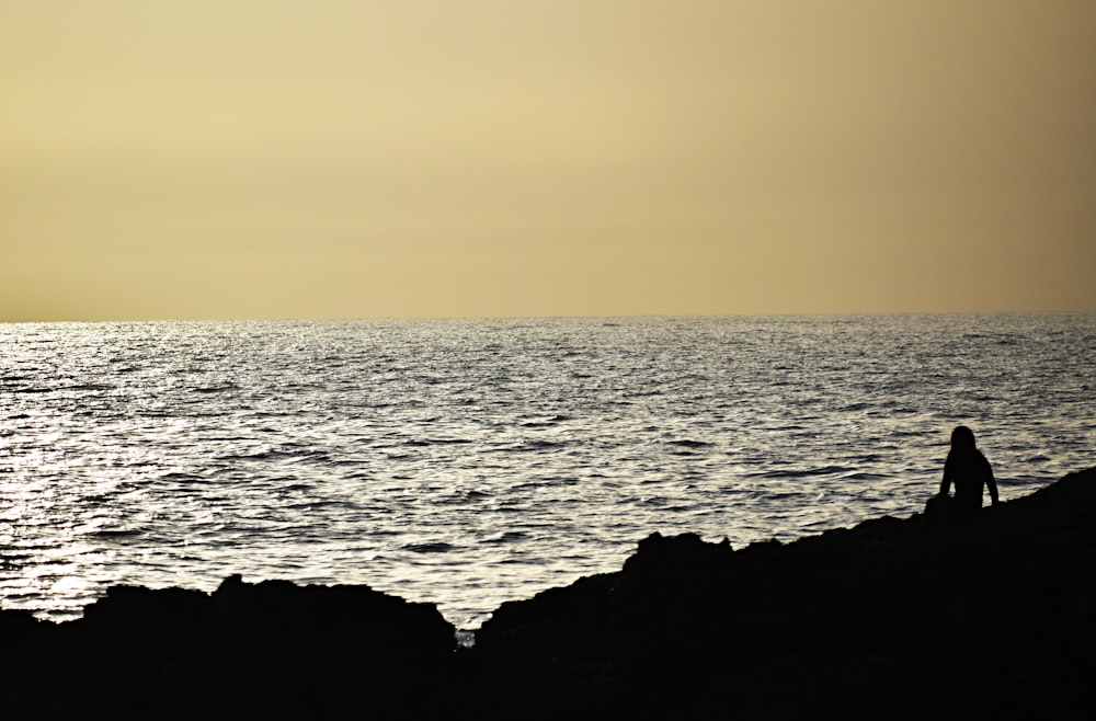silhouette of person sitting in front ocean