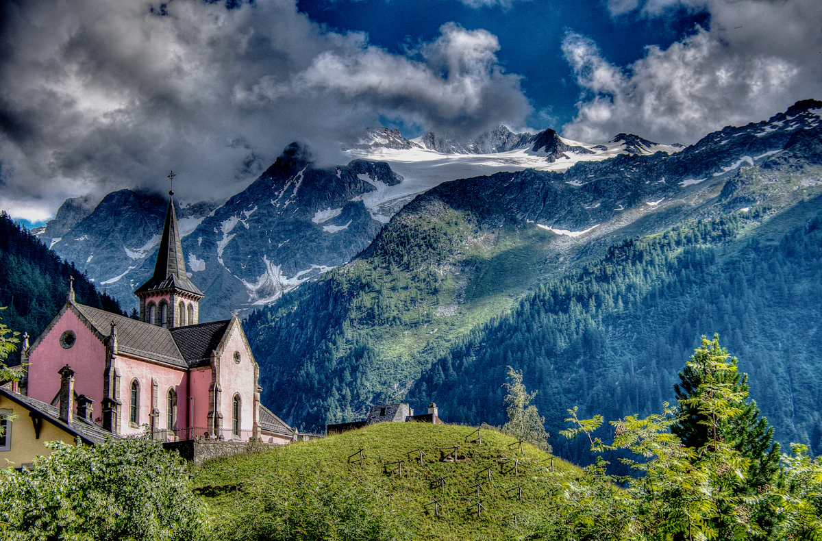 The pink church of Trient in Switzerland, with snowy peaks and green slopes behind