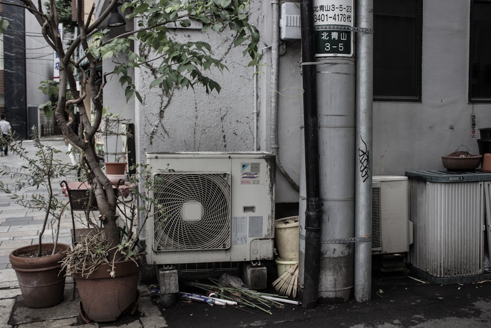 Luftkondensator neben zwei Topfpflanzen vor dem Gebäude