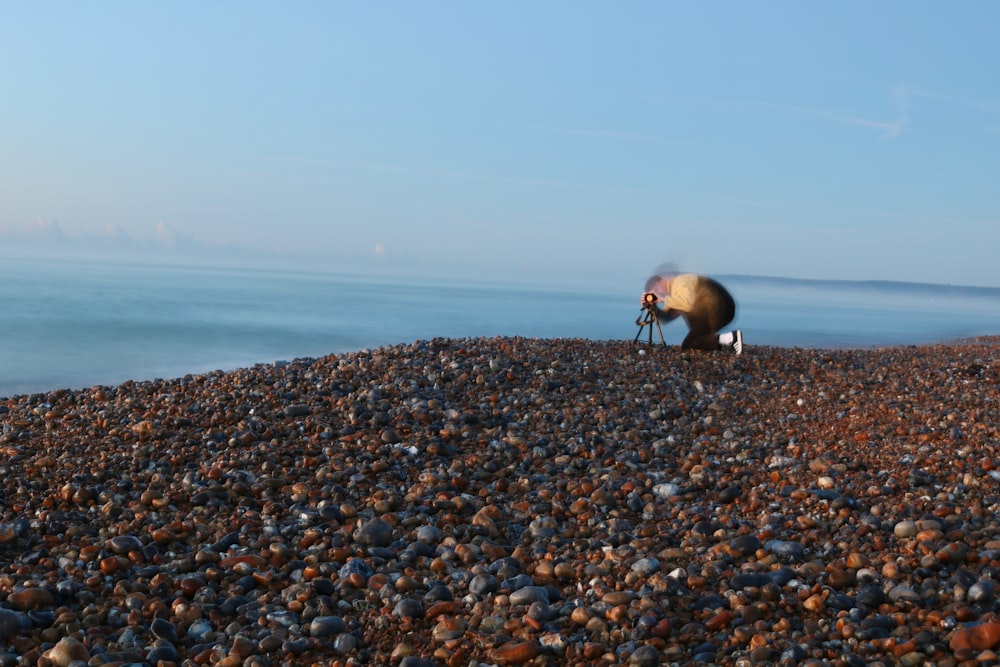 person holding tripod on brown stones near blue sea during daytime