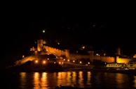 A view of the donjon’s exterior at dusk, with warm lights glowing through narrow windows.