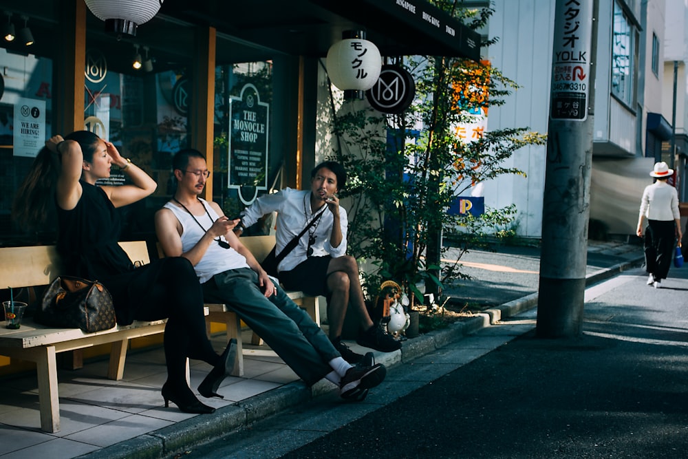 Drei Personen sitzen auf einer Bank vor der Straße