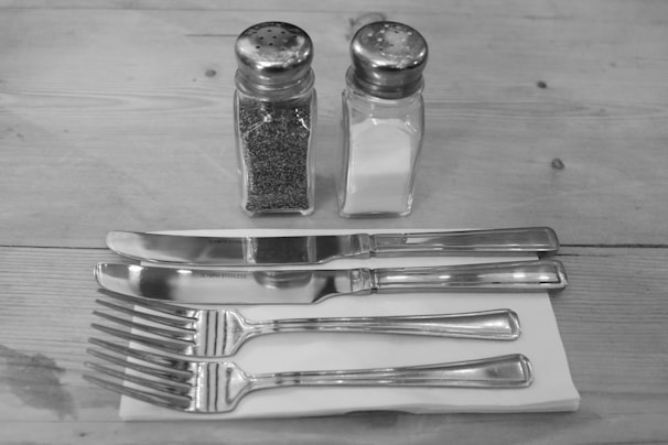 Close-up of an open drawer at a table showing neatly arranged cutlery, napkins, salt, and pepper.