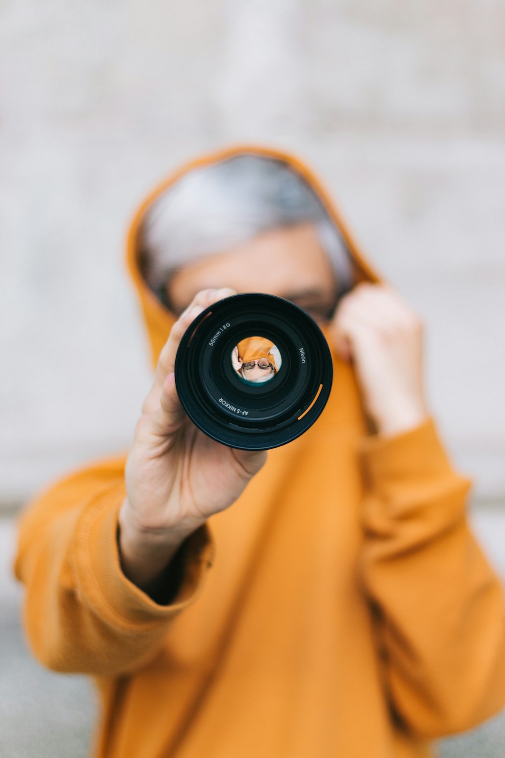 view of person in yellow hoodie holding camera lens