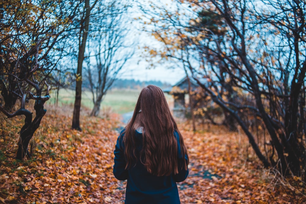 裸の木のそばの未舗装の道を歩く女性