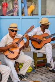 two men sitting on a bench playing guitars