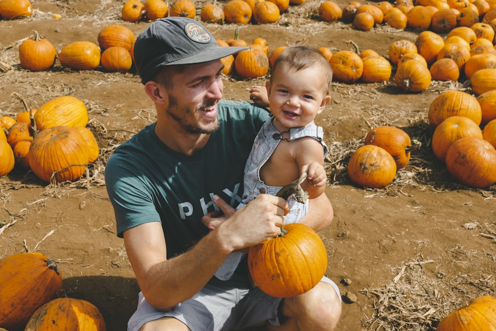 hombre sonriente que lleva a un niño pequeño mientras sostiene calabazas