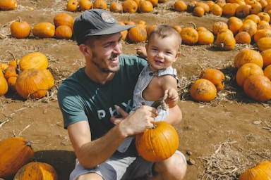 photography poses for family,how to photograph falling all over the pumpkins; smiling man carrying toddler boy while holding pumpkins