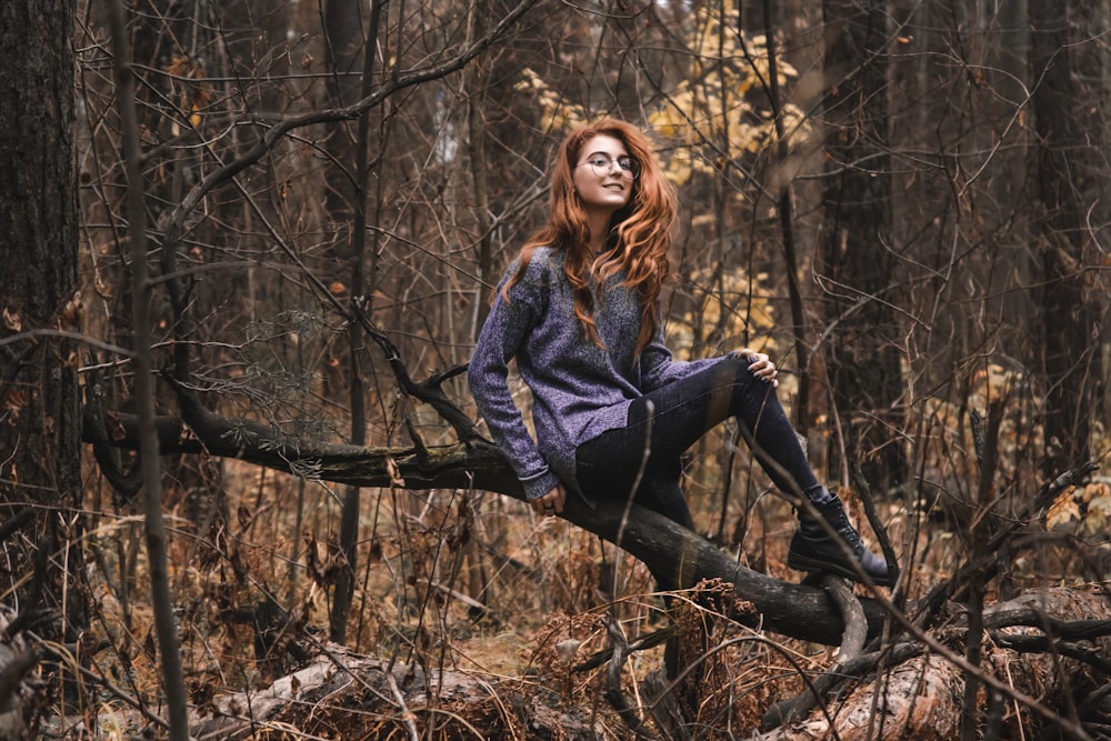 woman in gray and purple sweatshirt sitting on tree truck in forest during daytime