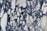 A marble surface displaying intricate black and white veining patterns with a few subtle hints of green. The design features irregular, jagged shapes interwoven amidst a backdrop of creamy white.