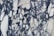 A marble surface displaying intricate black and white veining patterns with a few subtle hints of green. The design features irregular, jagged shapes interwoven amidst a backdrop of creamy white.