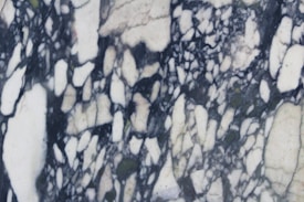 A marble surface displaying intricate black and white veining patterns with a few subtle hints of green. The design features irregular, jagged shapes interwoven amidst a backdrop of creamy white.