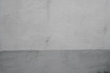 A textured concrete wall displaying a subtle two-tone gradient. The top part of the wall is a light gray while the bottom is a slightly darker shade. Minimalistic in style, the surface features small imperfections and marks.