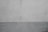 A textured concrete wall displaying a subtle two-tone gradient. The top part of the wall is a light gray while the bottom is a slightly darker shade. Minimalistic in style, the surface features small imperfections and marks.