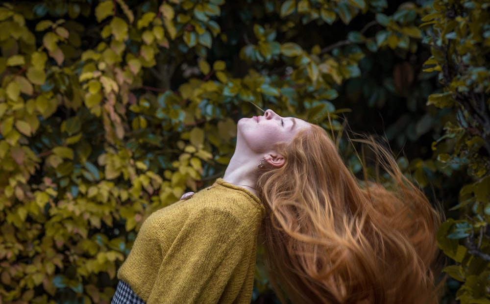 woman wearing brown crew-neck shirt standing in front of green leaves