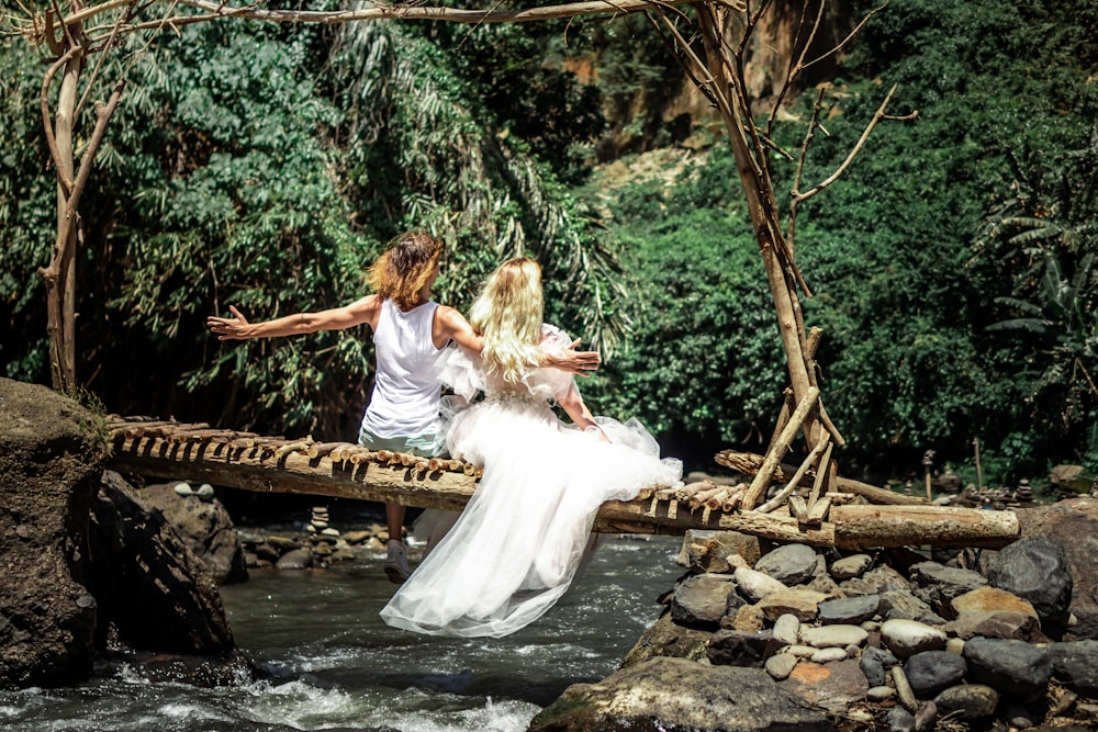 two woman sitting on tree branch above river during daytime