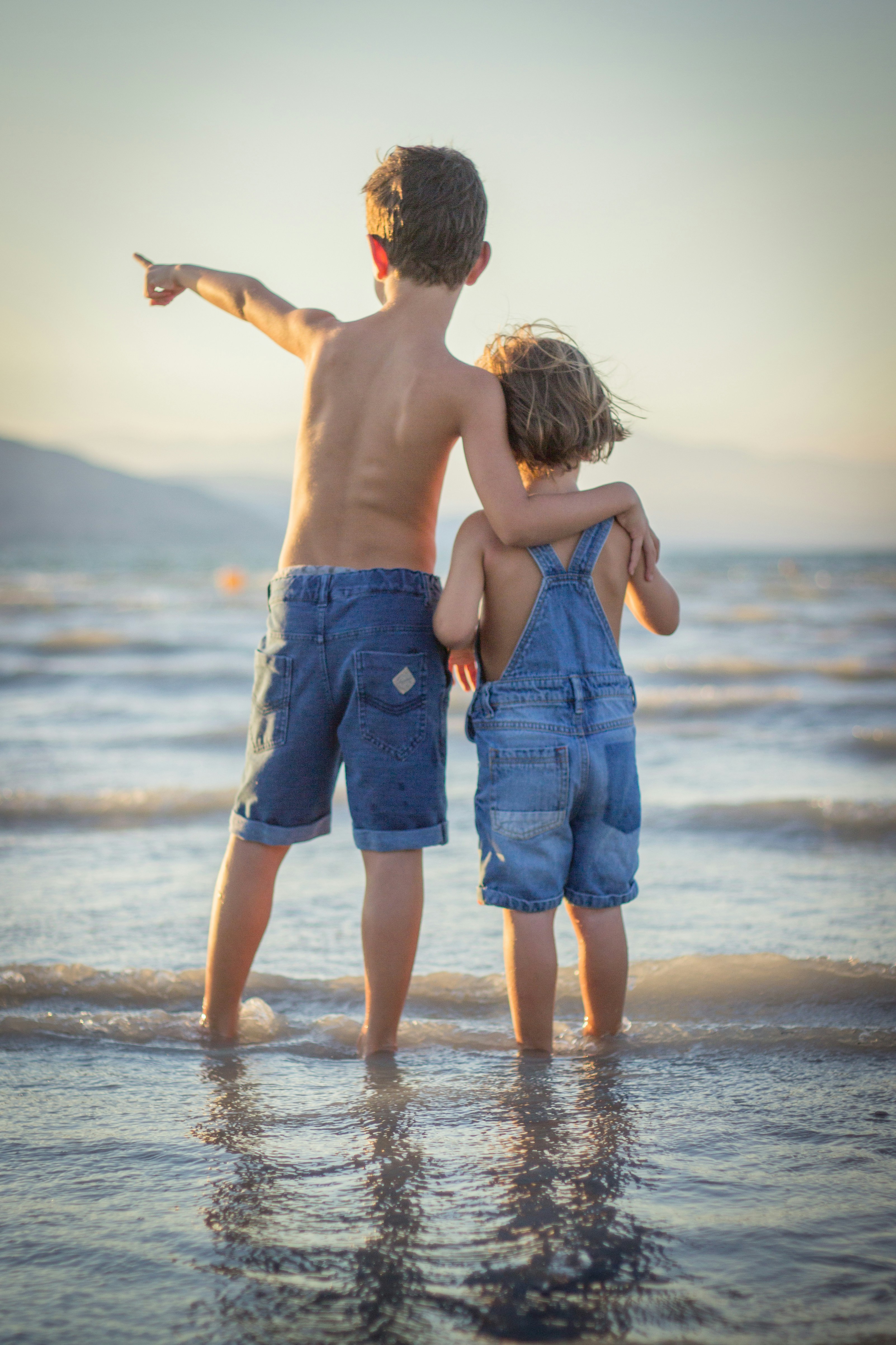 Young boy in jean shorts with arm around sibling at beach