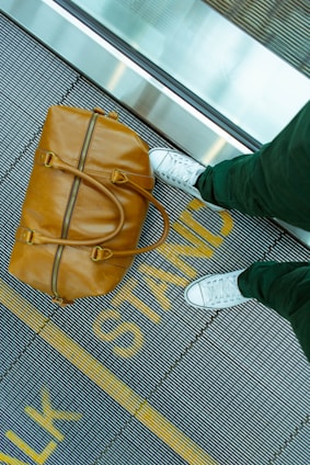 person stranding beside brown leather handbag