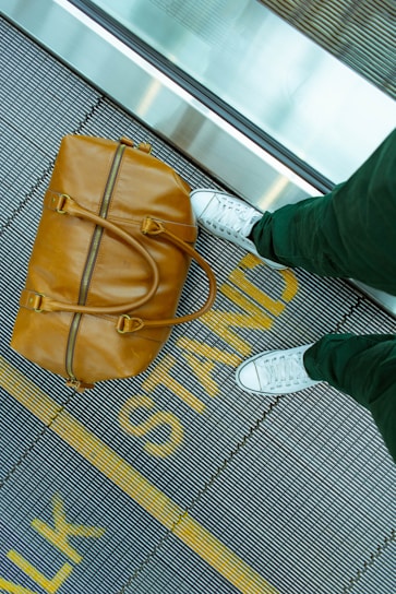 person stranding beside brown leather handbag
