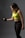 A woman is exercising with a dumbbell. She is wearing a bright yellow sports top and black leggings, focusing on her workout in a dimly lit environment.