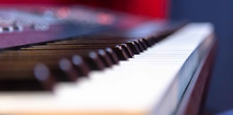 A close-up perspective of a piano keyboard with both black and white keys prominently displayed. The focus is on the keys, while the background is softly blurred, suggesting an intimate view of the instrument.