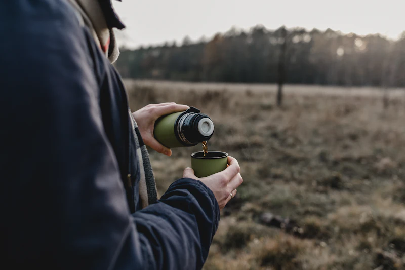 Hombre sirviendo café de un termo en plena montaña