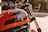 A close-up view of a motorcycle with an orange fuel tank featuring the brand name and decorative elements. The handlebars, mirrors, and parts of the chrome fork are visible, with a blurred background indicating an outdoor setting.