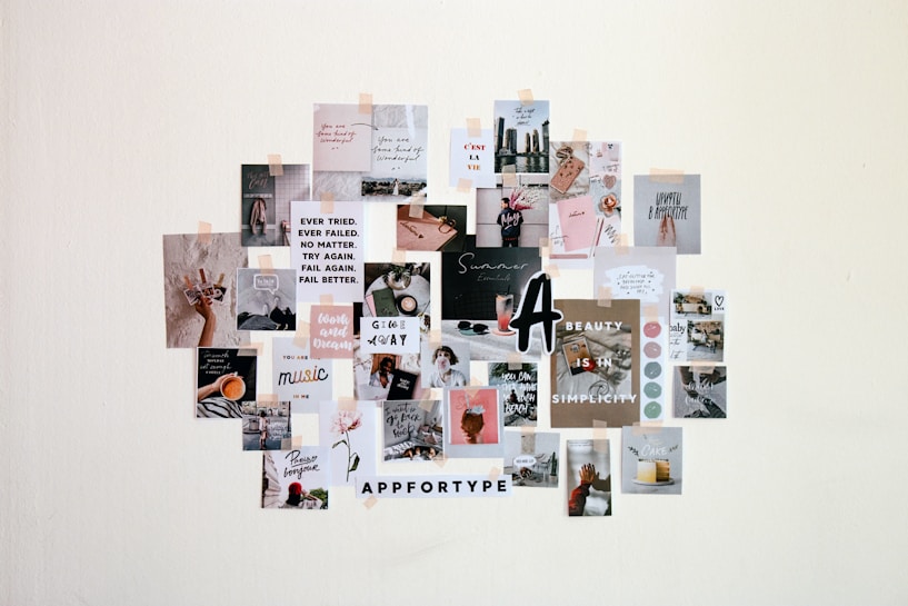 A collage of various small printed pictures and motivational quotes taped to a wall, showcasing a mix of lifestyle, fashion, and inspirational themes. The arrangement includes text-based posters with positive messages, aesthetically styled images of objects like coffee cups, flowers, and cityscapes.