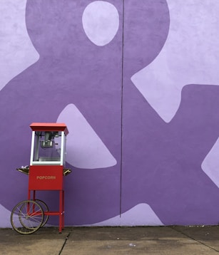 red and white popcorn cart beside purple wall