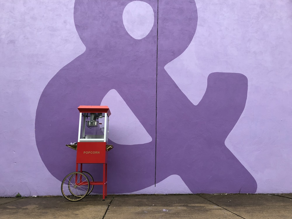 red and white popcorn cart beside purple wall