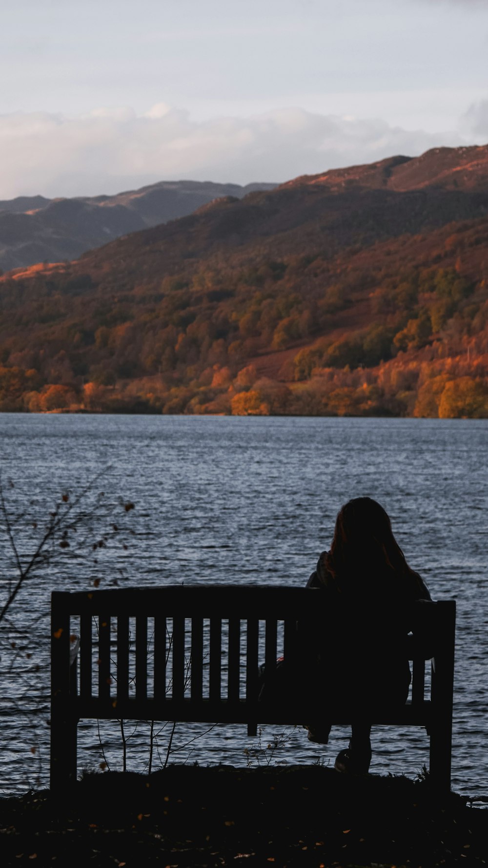 pessoa sentada no banco de madeira preto perto do corpo de água durante o dia