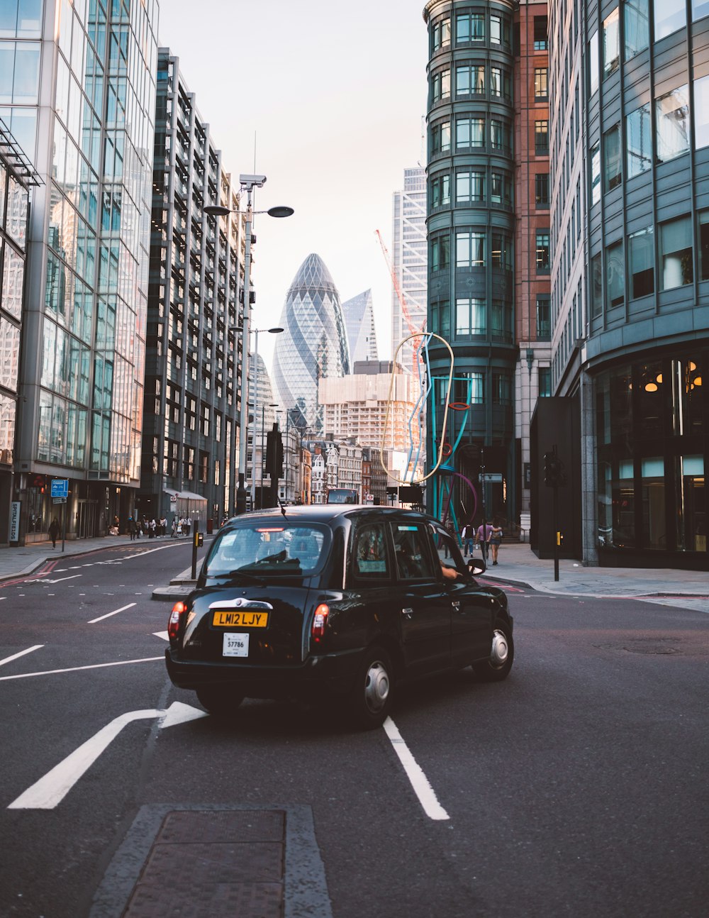 classic black car making right turn beside glass curtain buildings during daytime