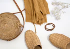 Minimalist flat lay of everyday essentials including soft beige and ivory tops with handcrafted accessories on a warm cream background.
